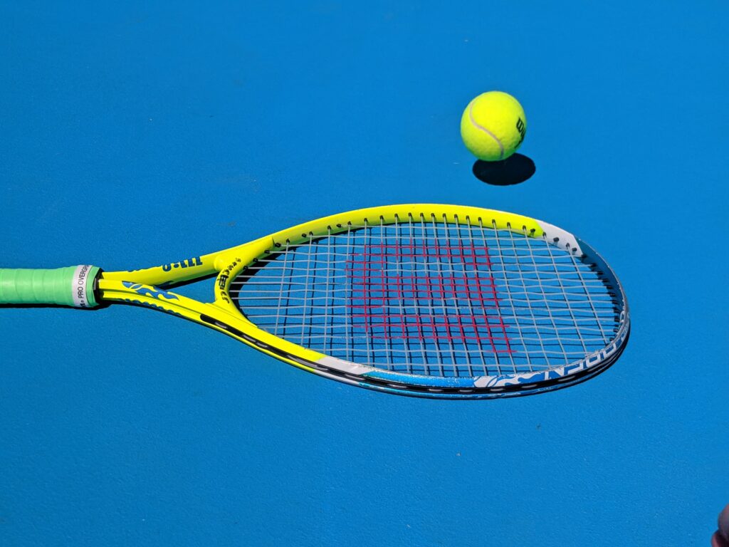 Ett tennisracket och boll på marken.